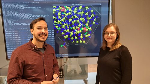 Lukas Hückmann (left) and Emilia Olsson (right) pose smiling in front of a screen displaying a computer model of a molecular structure.