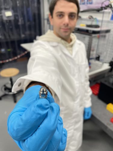 Enrico Pedretti holds out a diamond-coated sample for a closer look. He is wearing a white lab coat and blue gloves.
