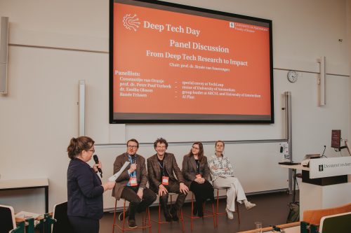 Panel discussion "From Deep Tech Research to Impact." Photo shows the 4 panelists, the chair of the session, and a projected slide with the details of the panel session.