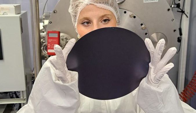 Linda Carano in the lab wearing cleanroom personal protective equipment and holding a silicon wafer.