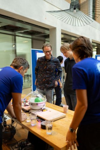 Two visitors watch as volunteers demonstrate what happens to a partly inflated balloon in a vacuum chamber as the pressure goes down.