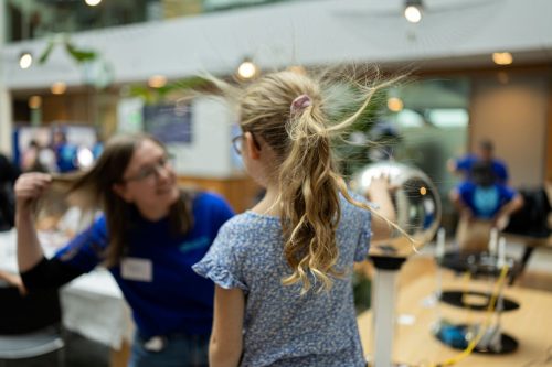 A young girl's hairs go up as she holds her hand to the Van de Graaff generator at the Wetenschapsdag.